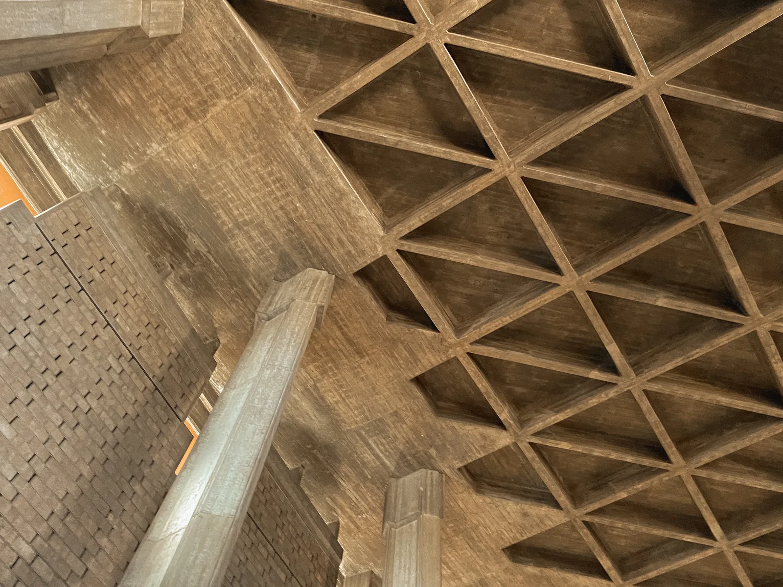 Exposed concrete waffle-slab ceiling with triangular beam grid and a board-formed concrete column in a brutalist building interior