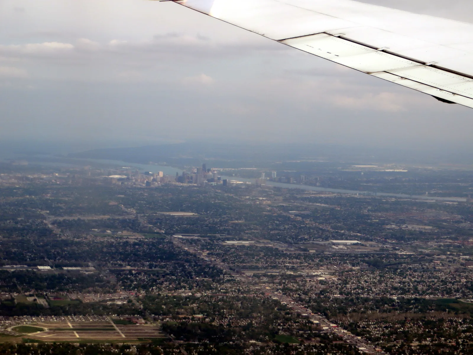 Hazy aerial city view beneath an airplane wing