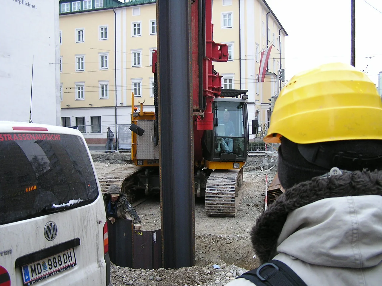 Worker in yellow hard hat watches tracked construction machinery