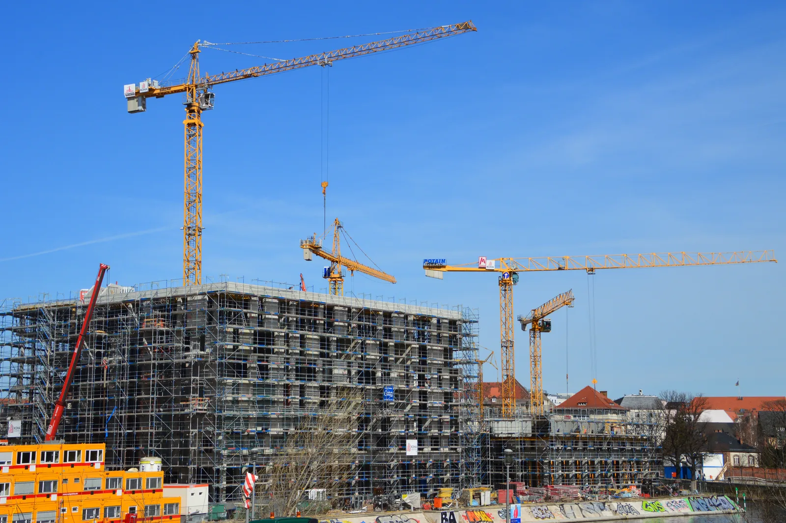 Tower cranes rise above a scaffolded multistory construction site