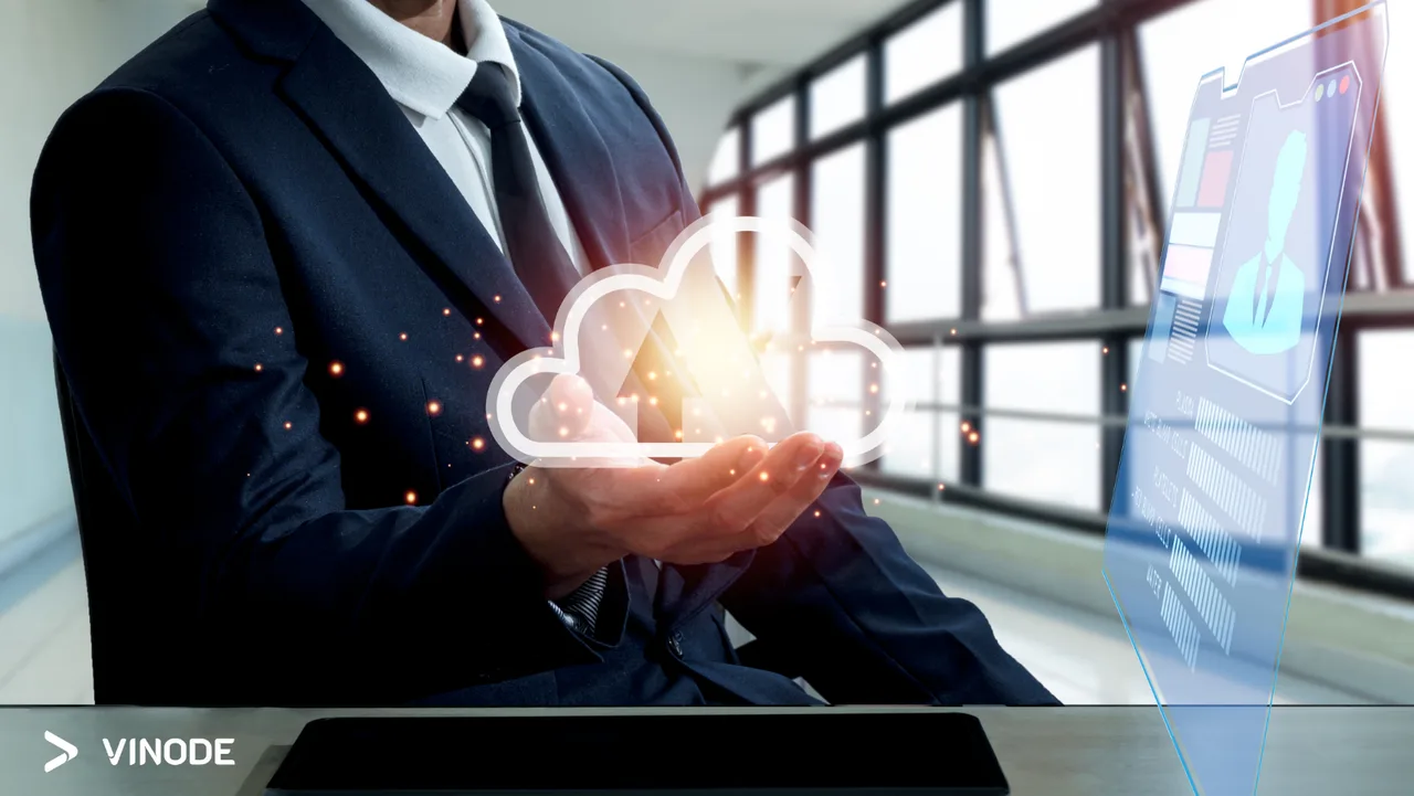 A businessman in a suit holding a glowing cloud icon beside a data screen